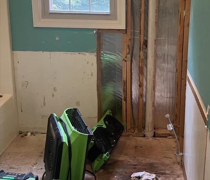 Part of a water damaged bathroom is shown with leaking around a toilet flange. Water is being dried up using green fans.