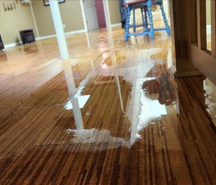 A wet wooden floor shows puddles from water damage.